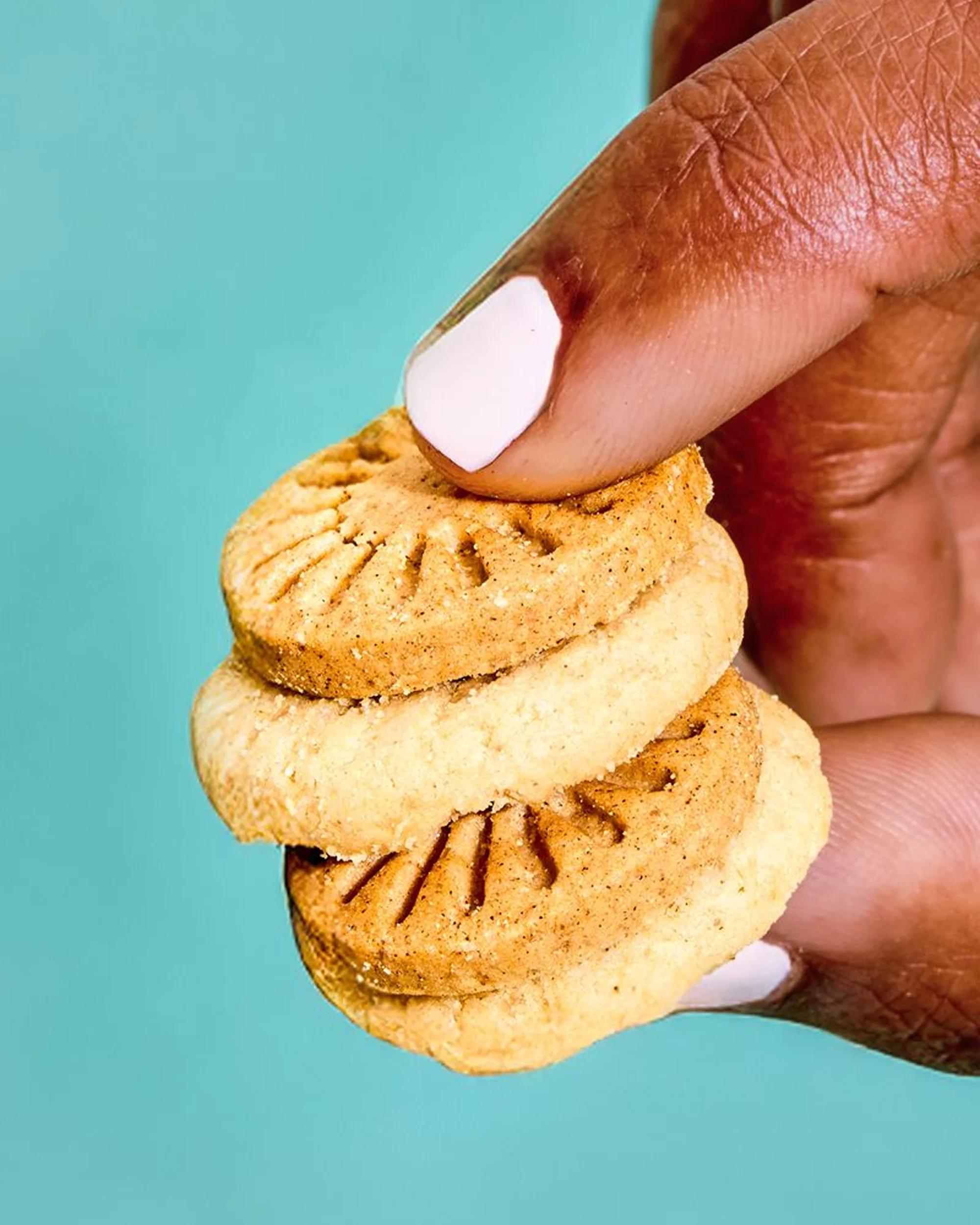 A hand holding a stack of mini vanilla wafers against a teal wall