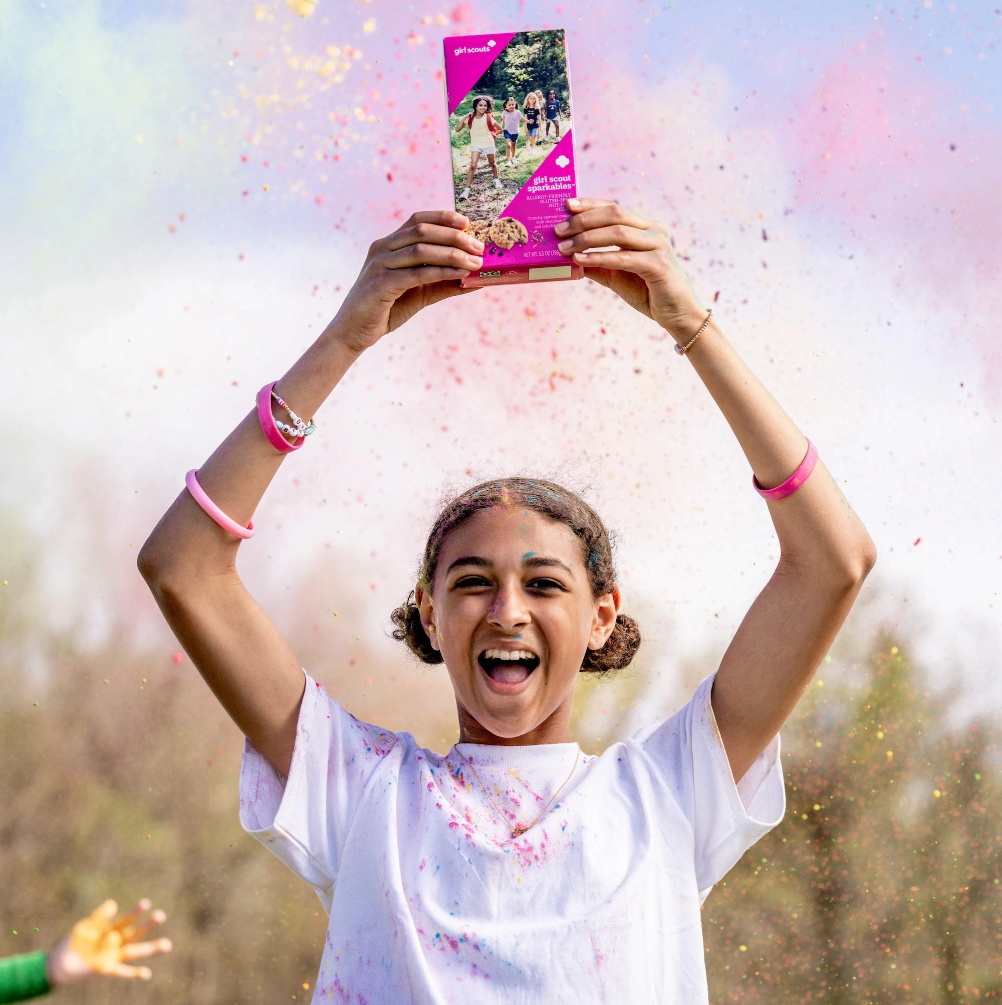 A girl throwing colorful confetti while holding up a box of cookies